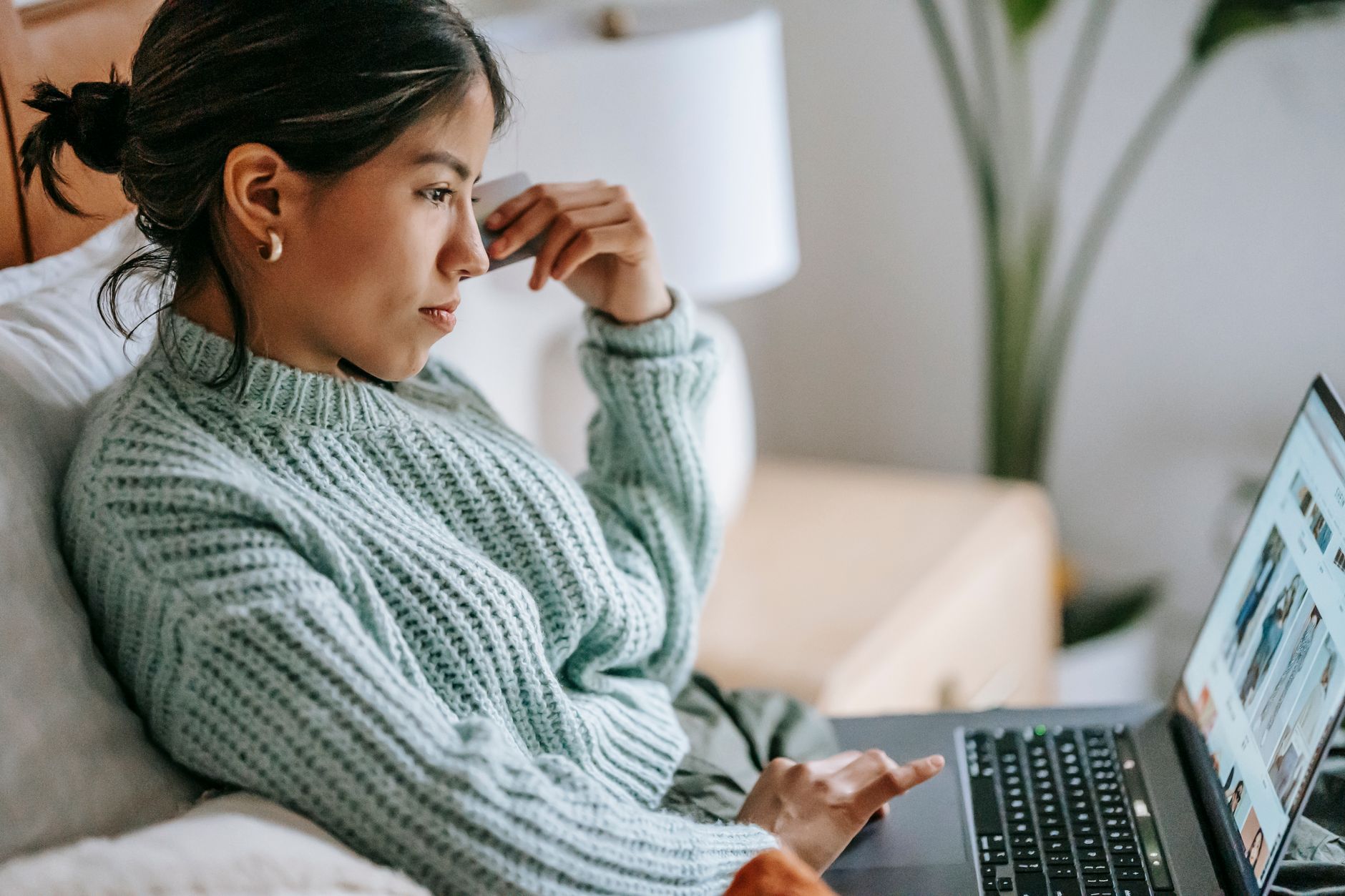 Una donna seduta su un divano guarda con attenzione lo schermo di un portatile mentre sfiora il touchpad.